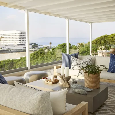 Wooden deck with modern beige outdoor sofas decorated with blue scatter pillows, a large coffee table and a circular wooden dining sit overlooking views of the beach and Beacon Isle. Walkers Beach Villa.