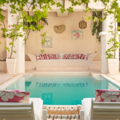 The Fort courtyard swimming pool decorated with plants, and surrounded by sun loungers and a built in sofa with floral scatter pillows.