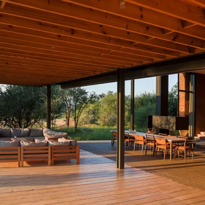 Witklipfotnein eco lodge outdoor seating with soft, grey corner sofas protected by a wooden pergola, and a long wooden dining table adjacent to the outdoor braai surrounded by the bushveld.