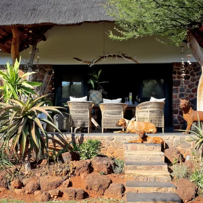 Beautifully thatched manor house with a blend of whitewashed walls and stone pillars, and a large deck in front of the house with dining table and woven wicker chairs.