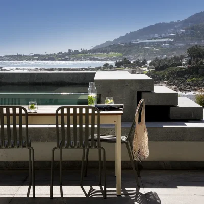 Ebb Tide's terrace furnished with a modern outdoor dining table and chairs that is positioned perpendicular to a terraced swimming pool that looks onto the ocean and slopes of Table Mountain.