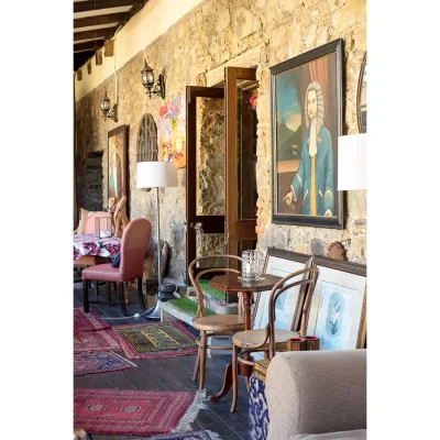 Living area in the Cape Heritage Hotel with high beamed teak ceilings, Cape yellowwood floors decorated with multiple Persian rugs, the original plasterwork with vintage artwork, and furnished with small wooden antique tables and chairs.