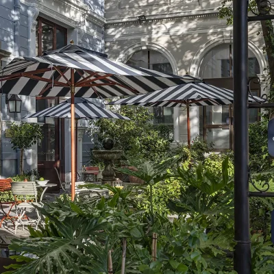 Labotessa Hotel entrance with Parisian Bistro style tables and chairs and black and white striped umbrellas surrounded by luscious green pot plants.