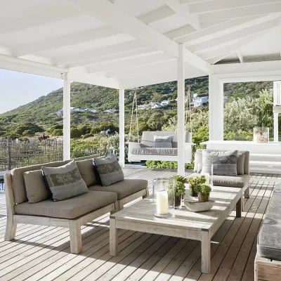 Noordhoek Beach House wooden deck with rustic wooden outdoor furniture and porch swing overlooking the swimming pool and surrounding views of Chapman's Peak mountain and ocean.