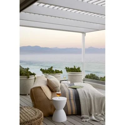 Large comfortable lounger with a soft beige blanket and side table positioned on Walkers Beach Villa patio with views of the ocean and distant mountain range.