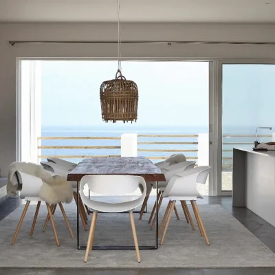 Unfettered dining area with a white finish unique to Feng Shui, with a large wooden dining table and hanging woven light that opens onto a mesmerising blue ocean via stacking glass doors.