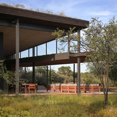 Outdoor and indoor spaces merge with an extensive elongated roof that protects the outdoor wooden dining table and braai area, and expands further with an outdoor lounging space protected by an attached pergola, and views of surrounding bushveld. Witklipfotnein eco lodge.