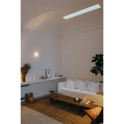 Living room in Casa Piana with white epoxy floors that match the white walls that curve toward the ceiling with a narrow skylight positioned above the woven rug with a wooden coffee table and large white linen sofa.