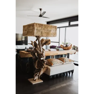 Sophisticated living area with a solid wooden console, a soft beige ottoman, and a ceiling fan with touches of quirkiness found in the lamp made of branches and animal fur. The Blogck.