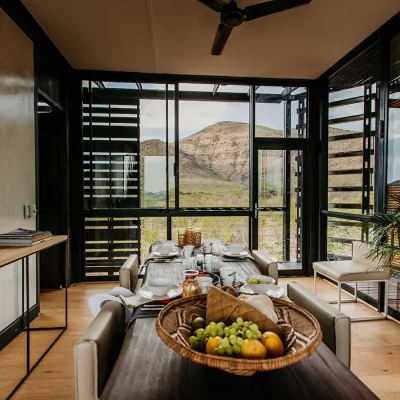 Dining area with beige washed walls, extended wooden table, leather chairs and wooden cabinet with views of the mountain from large glass windows.