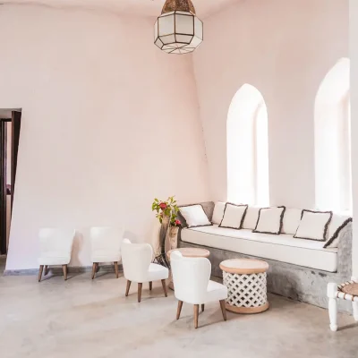 Secluded open plan lounge with whitewashed walls that compliment the compact white leather armchairs and built in sofa with soft, white pillows set against arched windows that bring ample light. The Fort.