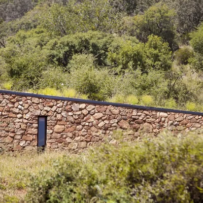 Elongated structure at Witklipfontein eco lodge with stone walls set amidst overgrown bushveld.