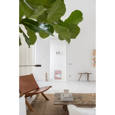 Casa Piana living room with a burnt orange leather chair, woven rug and wooden coffee table facing a white washed wall with open doorways.