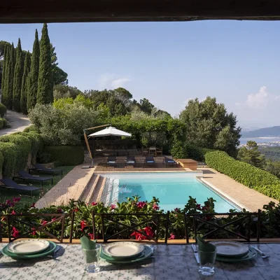 View of the swimming pool, forested slopes and ocean from the terrace of Villa Sunshine that is furnished with a set outdoor dining table.