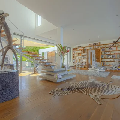 Open plan lounge with book case, armchairs, a zebra carpet, two statues and a modern staircase.