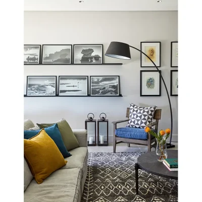 Contemporary lounge decorated with coastal wall prints, an arched standing lamp, a couch with scatter pillows and an armchair.