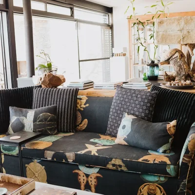 Open plan living area with large stack back doors, and a decorative black sofa and scatter pillows set against a wooden console with a quirky lamp and a wooden glasses cabinet in the background. The Blogck.