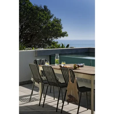 Ebb Tide terrace with modern outdoor dining set is decorated with a glass water dispenser, glasses and a cheese board, and positioned alongside a raised swimming pool with surrounding views of the crystal, blue ocean and a luscious corner tree providing subtle shade.