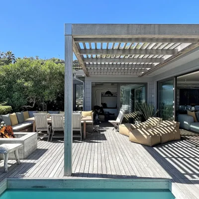 Oasis on Glen glass stack back doors opening onto the deck with outdoor furniture shaded by a wooden pergola, and a built in fire pit.