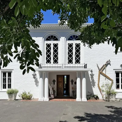 Face of Villa Toscana with exposed whitewashed brick walls, white columns and double wooden doors, arched windows and large wooden sculptures.