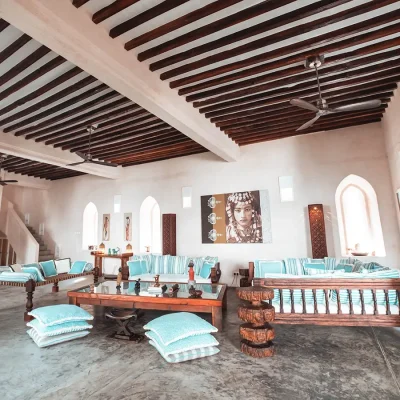 Traditional wooden sofas decorated with blue and white scatter pillows and surrounding a large glass coffee table in the Fort's open plan lounge in with whitewashed walls, arched doorways and wooden beam ceilings with built in fans.