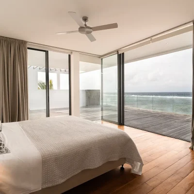 Second level contemporary bedroom with double bed overlooking deck and ocean via open, glass sliding doors.