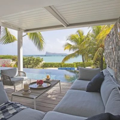 Covered outdoor lounge with panoramic views of the infinity pool, palm trees and blue ocean hues.