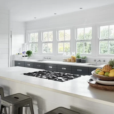 Noordhoek Beach house kitchen with white cladded walls and 5 consecutive windows exposing a flood of light on the white granite counters with charcoal cabinets.