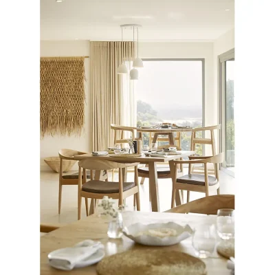 Dining space in Walkers Beach Villa with modern wooden tables set with sleek wooden chairs overlooking the ocean via large glass doors.