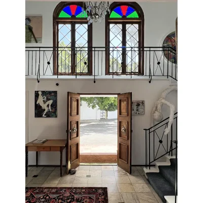 Grand entrance hall of Villa Toscana with double wooden doors, art sculptures and a wrap around staircase to the second level with large stained glass windows and a chandelier.