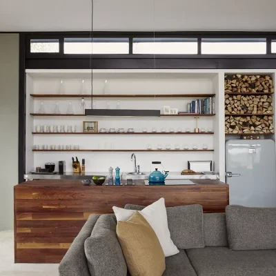 Contemporary kitchen in the Herenberg with solid wooden kitchen island and a sleek, built-in wooden cabinet storing glasses that is positioned alongside a Smeg Fridge that is surrounded by a wood stacked wall.