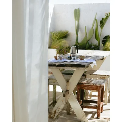 Outdoor patio with a rustic white wooden table and stools and enclosed by whitewashed walls with surrounding succulents. Casa Piana.