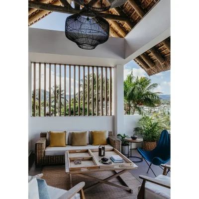 Lounging area on the terrace with a woven sofa and soft, beige pillows, and natural light flooding through wooden slats in the wall of Black River Penthouse.