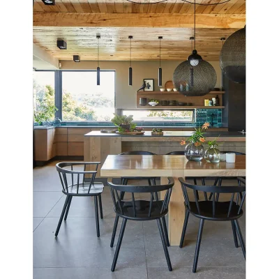 Open plan kitchen with glass-lined corner window overlooking greenery, and dining area with wooden table and chairs.