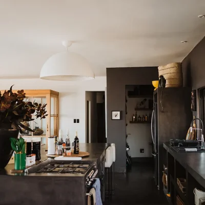 The Blogck kitchen with a lengthy kitchen island and built in gas stove, sleek charcoal counter tops and a built in pantry with matching charcoal walls.