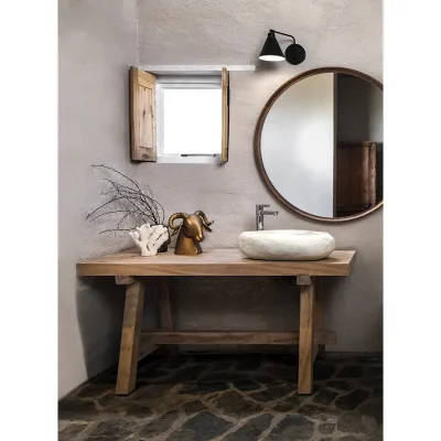 Bathroom with beige washed walls and stone floors, a mini window, a singular ceramic washbasin and a round mirror.