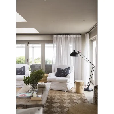 Two soft, white armchairs positioned in the midst of wraparound glass stack doors in Beach House Zonnestraal that is warmed by a woven floor rug and a rustic wooden coffee table.