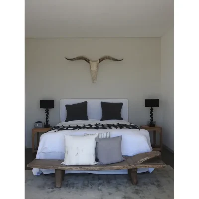 A tranquil bedroom with a double bed and white linen, wooden bedside tables and natural horns above the bed, with white and charcoal finishes. Feng Shui.