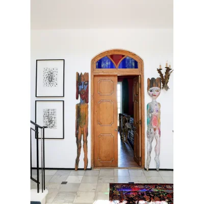 Hallway in Villa Toscana with marble floors exposed from the Persian rug, and two wooden statues that stand guard of the double wooden doors with arched stained glass.