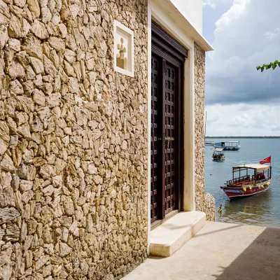 Peponi Hotel side pathway with stone walls and double wooden doors that open onto the calm ocean with wooden dhows.