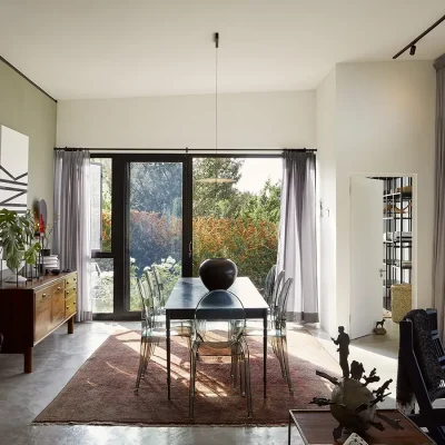 A Gregor Jenkins steel dining table and accompanying Ghost chairs positioned on a rustic, red Persian rug with views of the garden all make the Herenberg an elegant, flamboyant take on a farmhouse in the Free State.