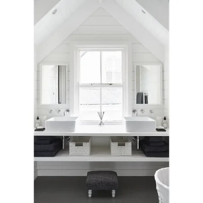 Noordhoek Beach House bathroom with twin ceramic washbasins and two mirrors mounted on the white cladded walls with a central window.