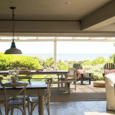 Open plan living room with wooden dining table in Beach House Zonnestraal that opens via stack-back doors exposing the verandah with additional outdoor seating and a view of the ocean.