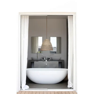 An elegant free standing white bath tub, with twin washbasins and mirrors, and a woven hanging light faces double doors that open onto the garden adding opulence to Feng Shui.