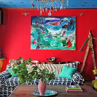 Living area with bright red walls, a blue ceiling with gold stars and furnished with a black and white sofa with tiger prints, wooden cabinets and a wooden coffee table with surrounding art pieces.