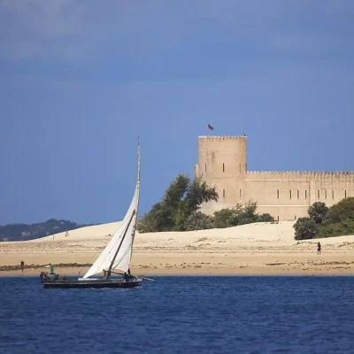 Deep blue ocean with a dhow sailing past The Fort situated on Shela Beach shoreline.