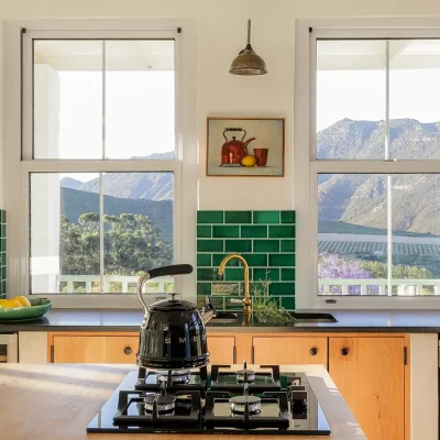 Kitchen island with built in gas stove and facing the green tiled walls with two large windows exposing the mountainous landscape. Buchubos Villa.