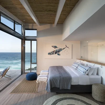 Bedroom suite in Lekkerwater Beach Lodge with a spacious bed and crisp white linen set against a floating wall that separates the open ensuite bathroom, and faces large stack back doors that reveal expansive views of the ocean.