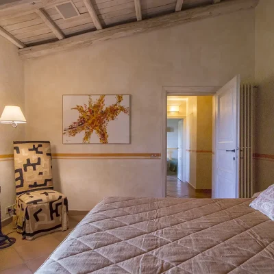 Bedroom with cream textured walls, simplistic artwork and a comfortable sized bed with pastel pink bedding, and a corner chair. Villa Sunshine.