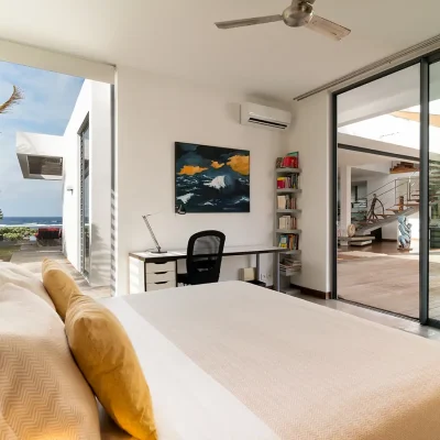 Bedroom on first level with desk, chair, wall art, and sliding doors opening onto back garden, and a large side view window of the ocean.